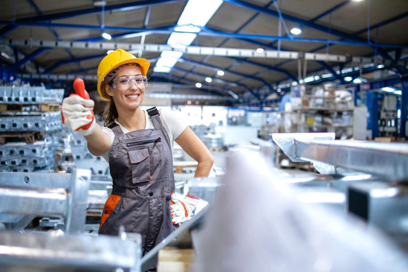 Female production line worker holding thumbs up in factory hall.